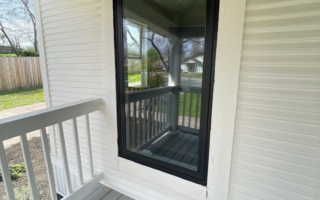 large picture window installation with black frame and white lap siding